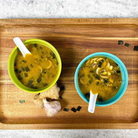 Blue and green bowl of miso soup on a cutting board