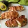 avocado stuffed bacon wrapped chicken on white platter with avocado in background