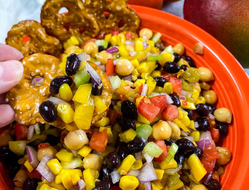 pretzels dipping into corn and black bean dip in an orange bowl