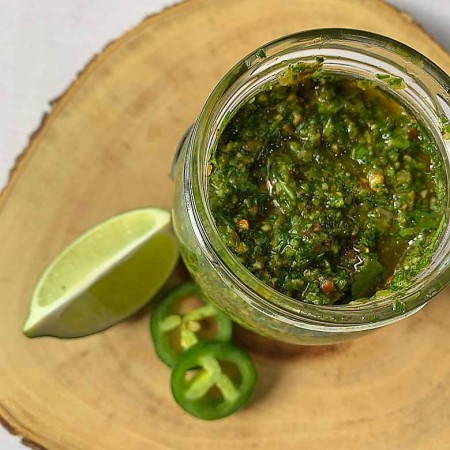 top down view of chimichurri sauce in a glass jar on a slice of wood