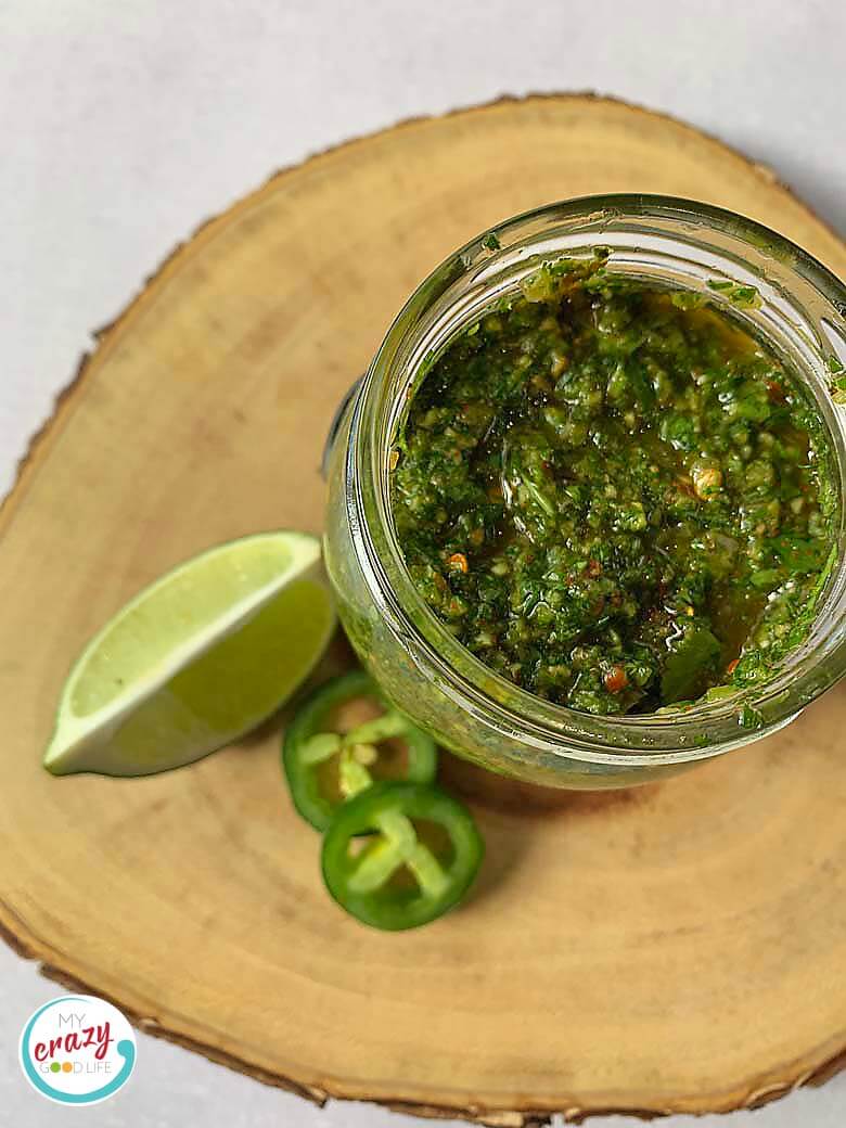 top down view of chimichurri sauce in a glass jar on a slice of wood