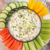 image of dill pickle chicken dip in a clear glass bowl with colorful dipping veggies