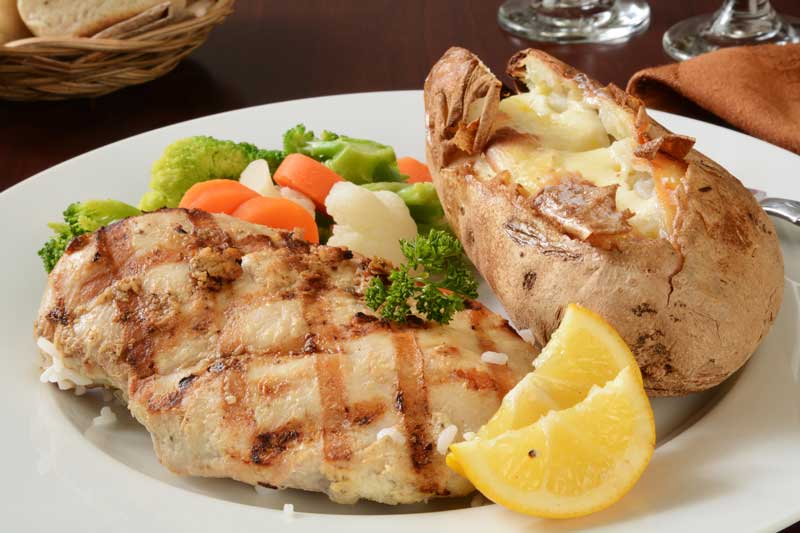 grilled chicken, vegetables, and a baked potato on a white plate