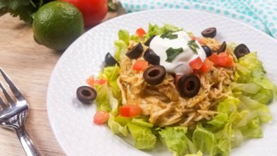 green chili chicken on top of a bed of lettuce with greek yogurt and olives on white plate