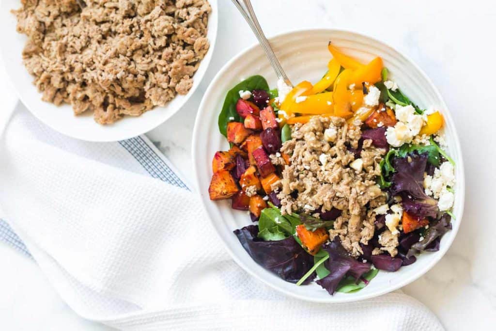 white counter with bowl of cooked ground turkey in the background, seasoned ground turkey as a salad topping in the foreground