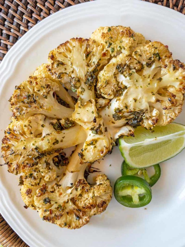 grilled cauliflower steak with lime and jalapeno on a white plate