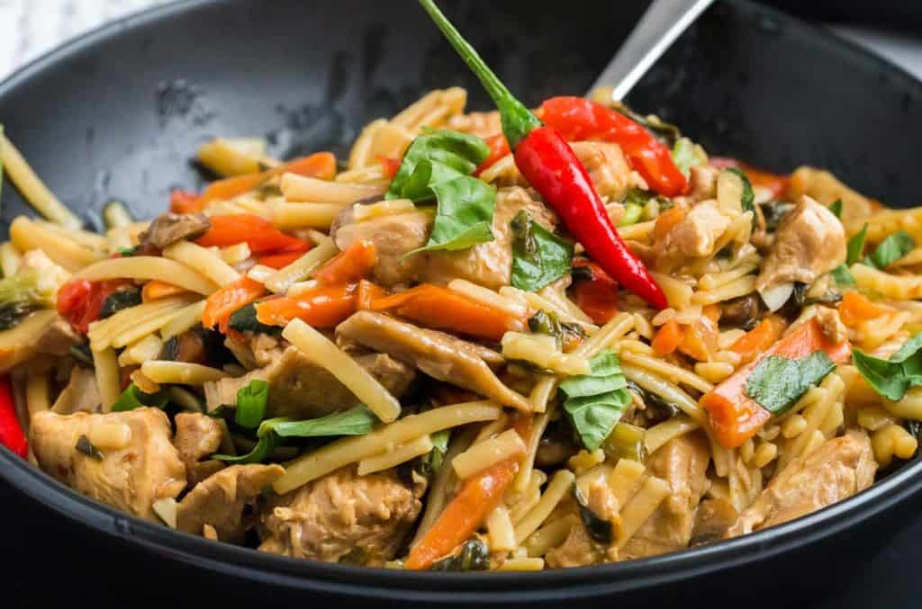 close up of cooked and plated drunken noodles in black matte bowl