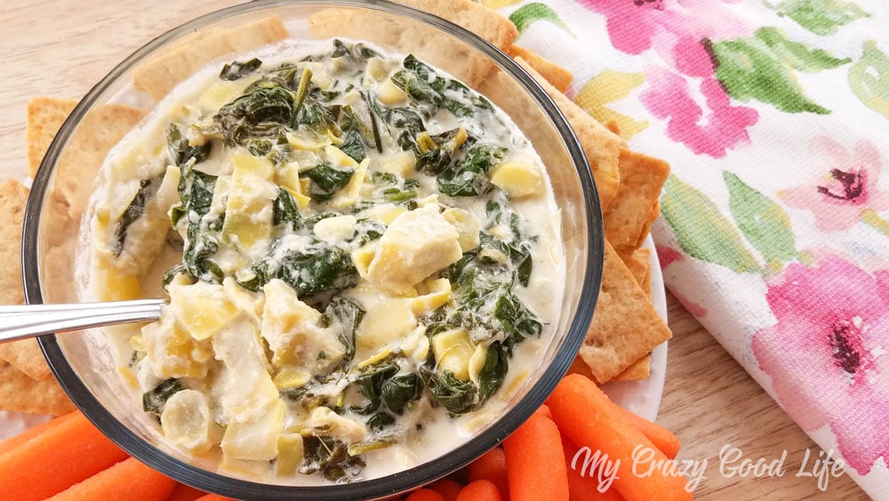 spinach and artichoke dip in a clear bowl with veggies