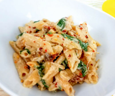 tuscan chicken pasta in a white dish close up shot.