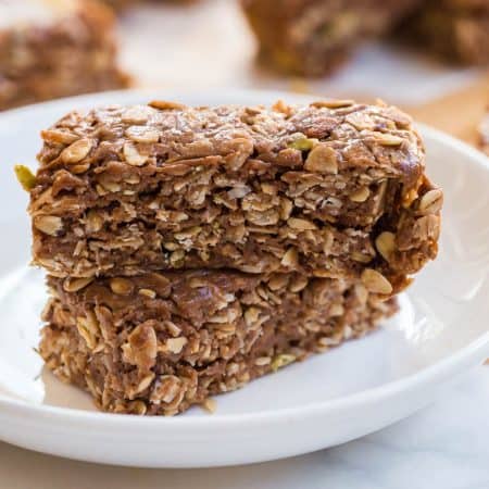 two homemade peanut butter granola bars on a white plate. in the background you can see more granola bars on butcher paper.