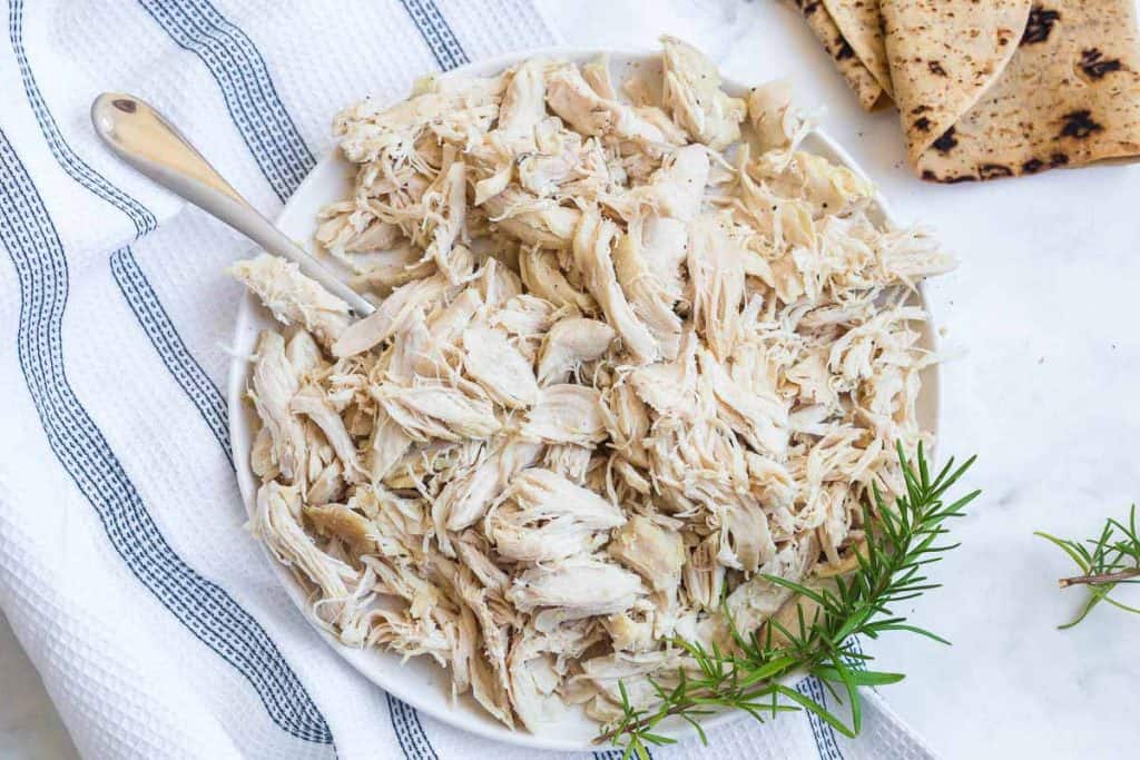 top down view of cooked shredded chicken with fresh herbs, wheat tortillas off to right side.