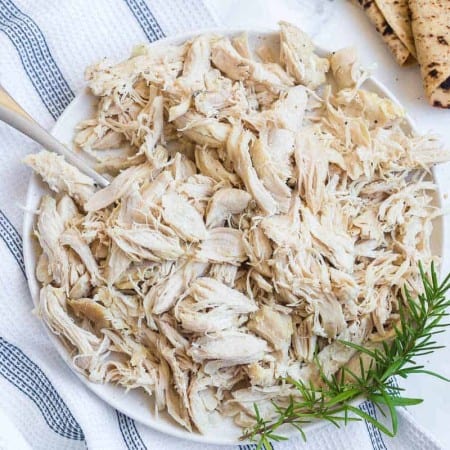 top down view of cooked shredded chicken with fresh herbs, wheat tortillas off to right side.