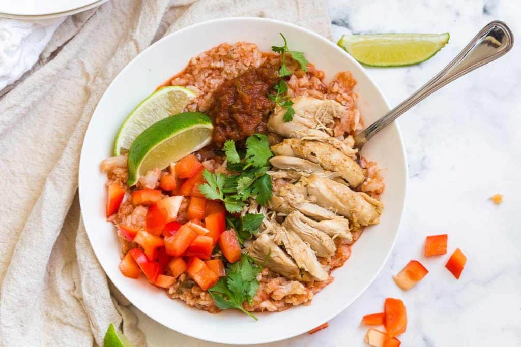 white counter with white bowl filled with cauliflower rice, shredded chicken thighs, and fresh vegetables