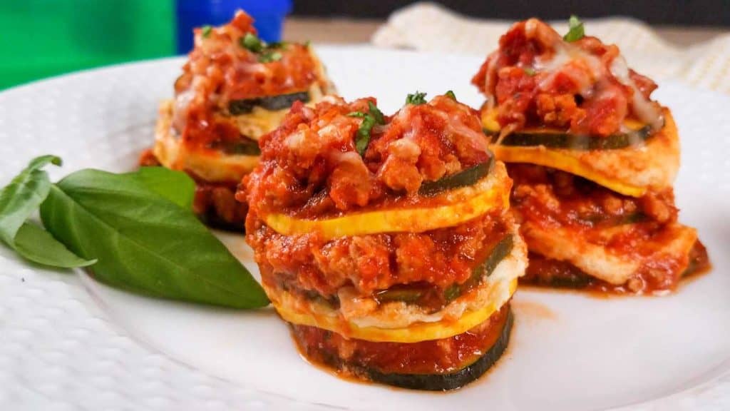 three mini lasagna bites on a white plate with fresh basil