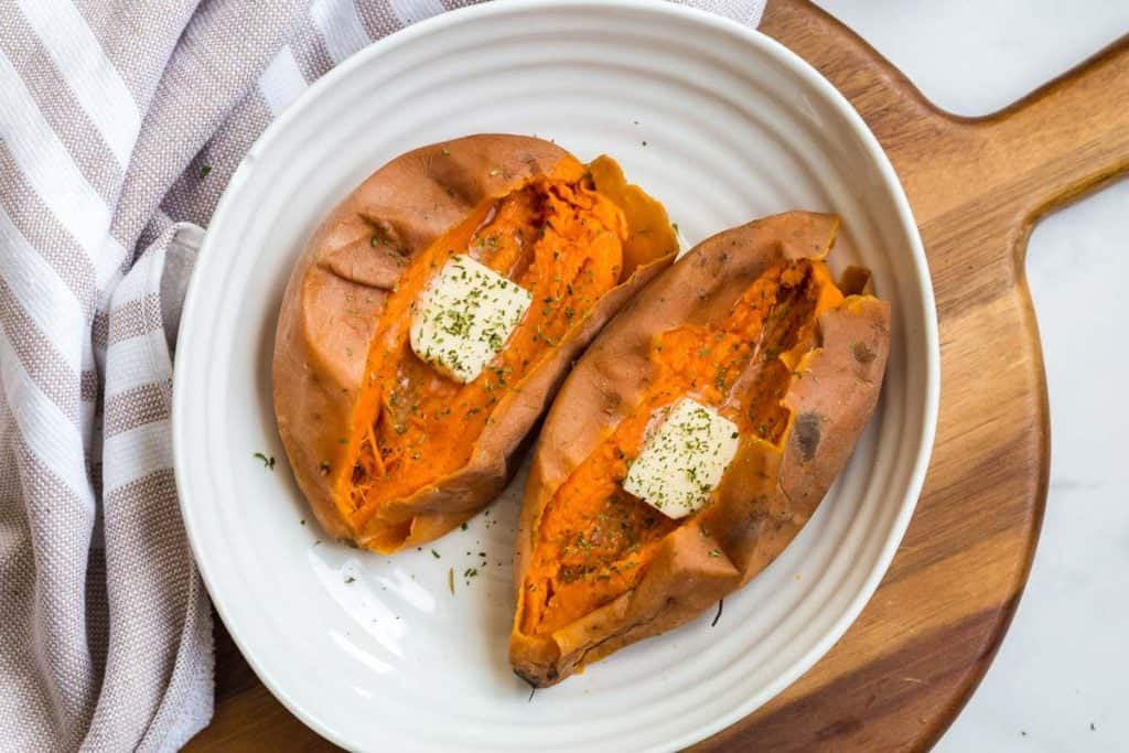 two cooked whole sweet potatoes, cut in half and dressed with butter and dried parsley.