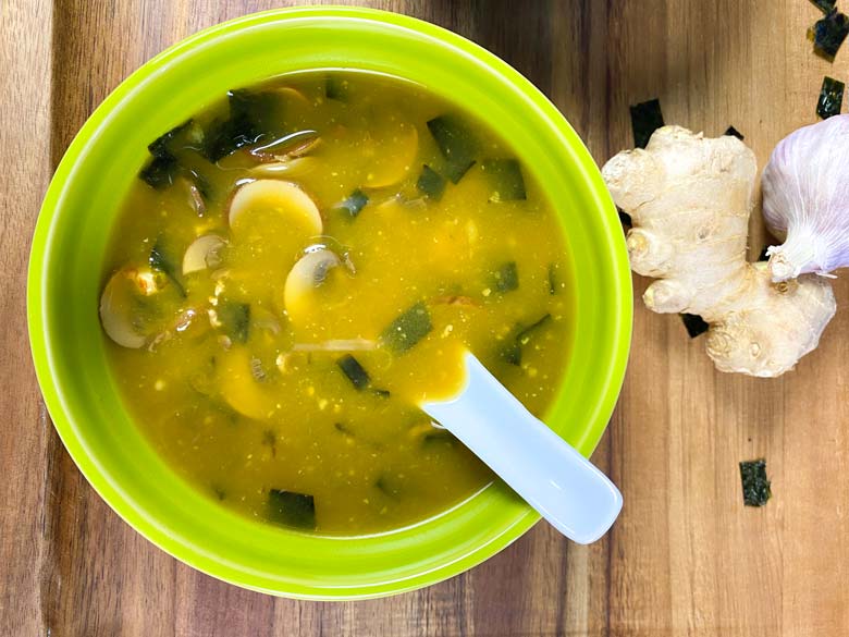 Close up of miso soup in a green bowl with fresh ginger and garlic