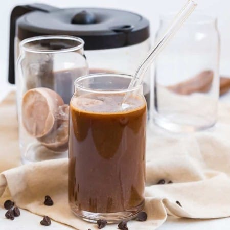 glass of iced coffee with mocha creamer ice cubes and coffee in the background