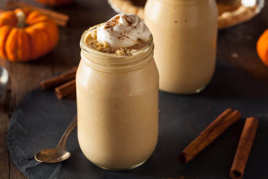 dark background with pumpkin milkshake in a glass mason jar. Shake has whipped cream and cinnamon decoration on top.