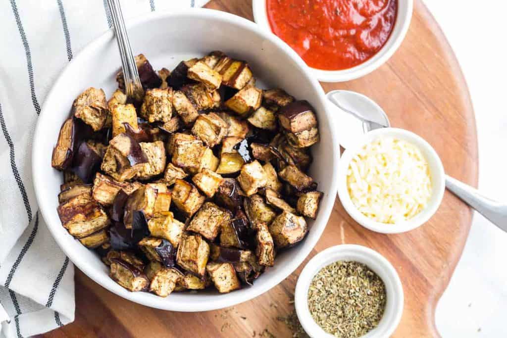 roasted eggplant cubes in bowl with seasoning and dipping sauce