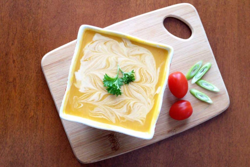 Soup in white square bowl on top of wooden cutting board.