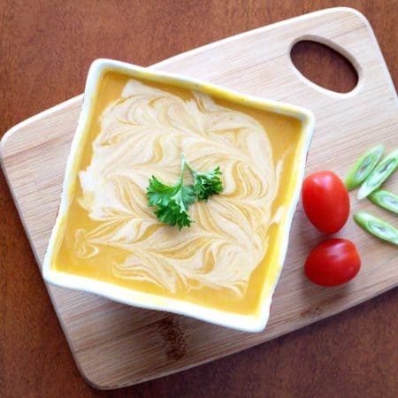 Soup in white square bowl on top of wooden cutting board.