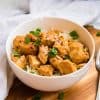 white bowl of Healthy Orange Chicken Recipe on top of a wooden board with white napkin and fork