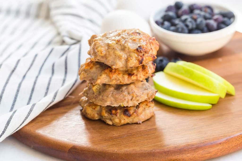 stack of four Sausage Patties on a plate with fruit in background