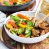 Teriyaki tofu stir fry bowls with coconut rice in a white bowl on a wooden cutting board