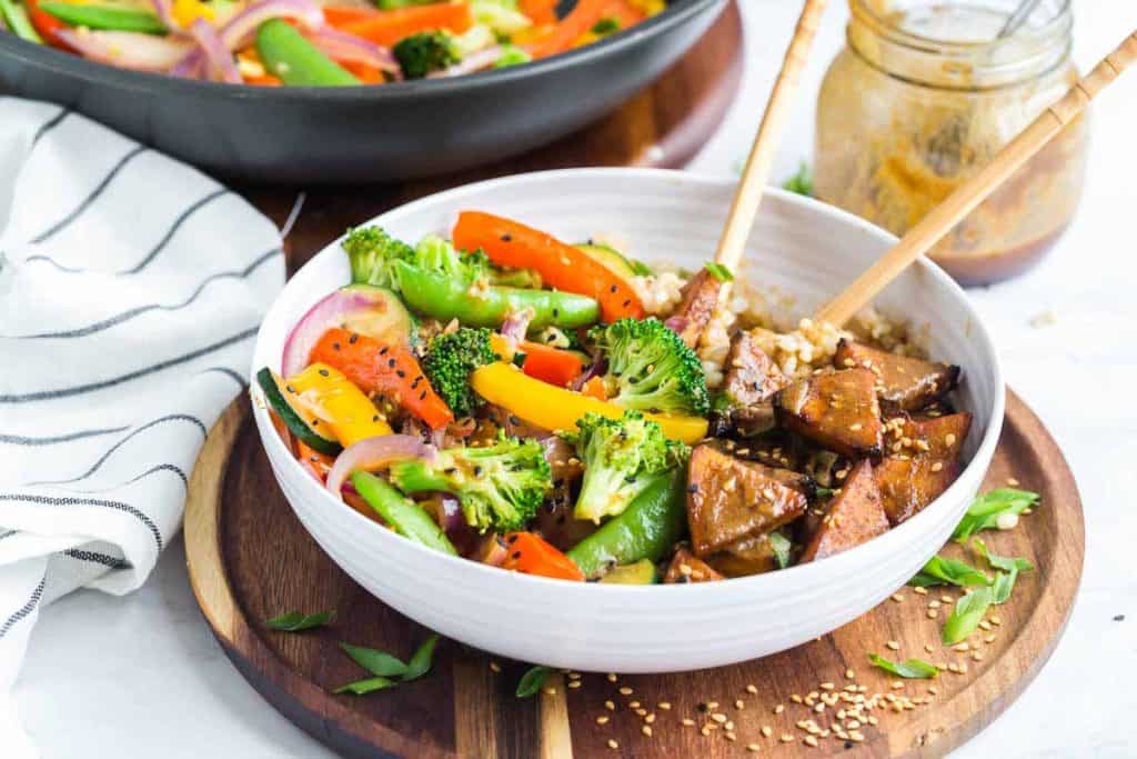 Teriyaki tofu stir fry bowls with coconut rice in a white bowl on a wooden cutting board