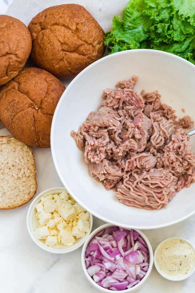 ground turkey in white bowl, wheat buns in top left corner, feta cheese, diced red onions, and ranch seasoning in white bowls 