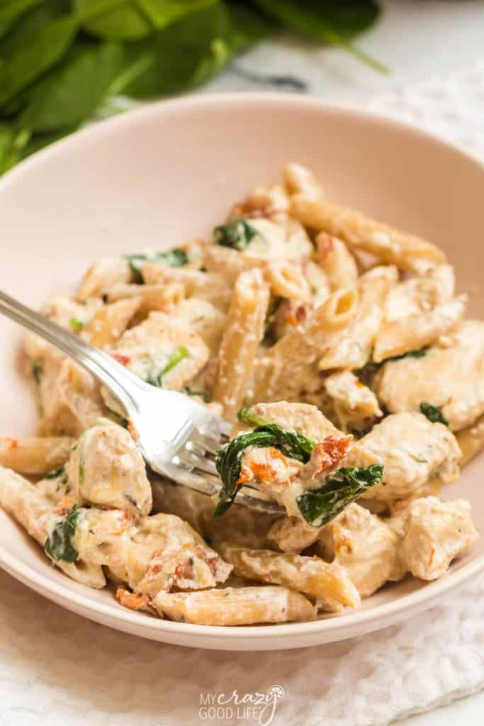 tuscan chicken pasta in white bowl with one fork full of food