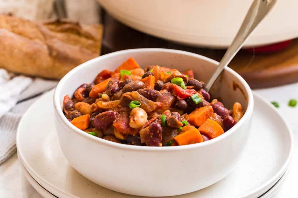 white bowl full of vegan chili, fresh bread in the background