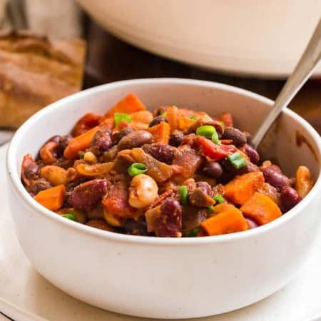 white bowl full of vegan chili, fresh bread in the background