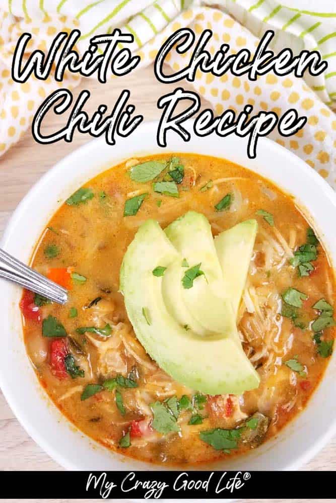 close up of cooked White Chicken Chili in a white bowl with sliced avocado on top